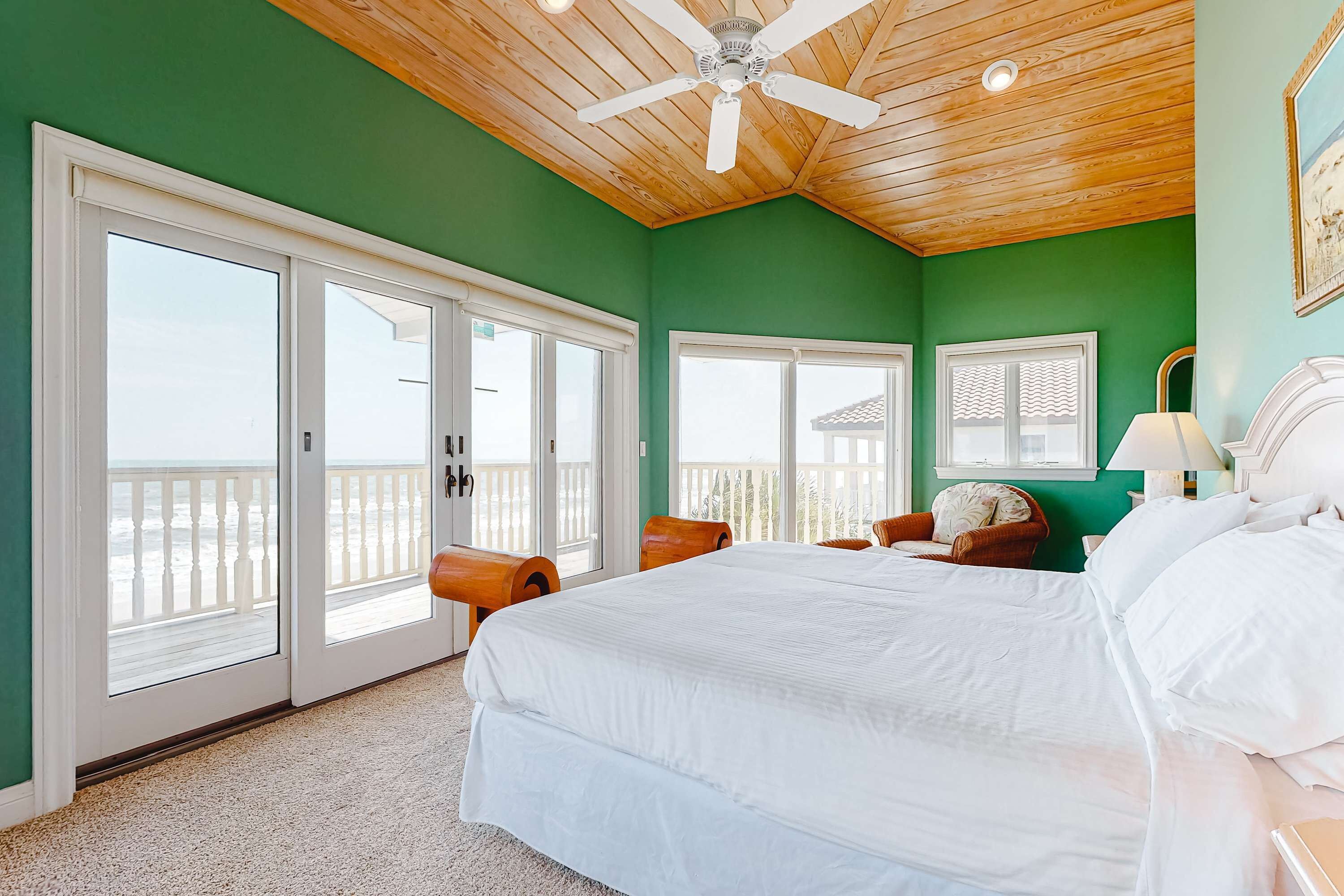 Un dormitorio con una cama grande, un ventilador de techo y vistas a la playa a través de puertas corredizas de vidrio.