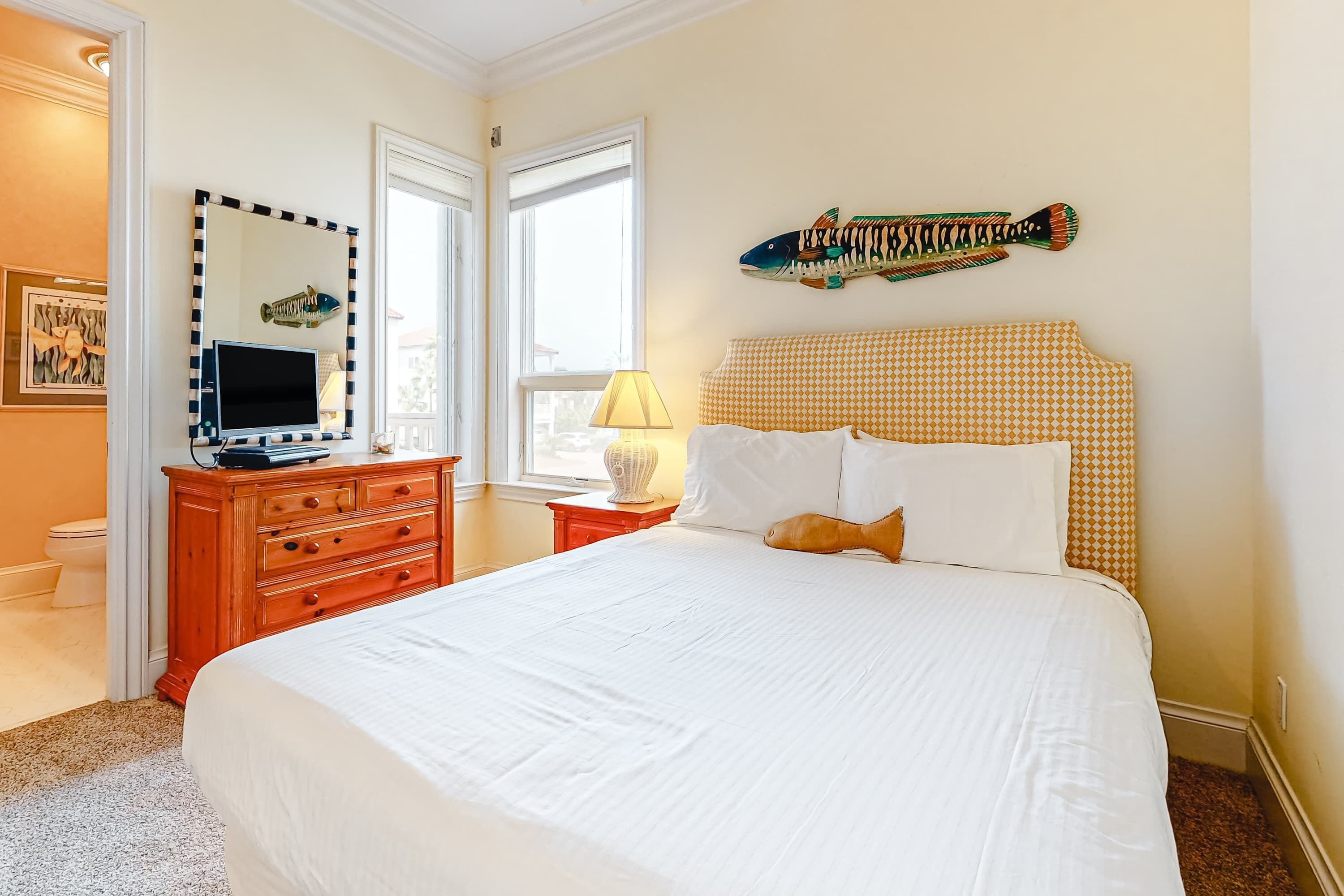 Ein Hotelzimmer mit einem großen Bett, einem Schminktisch, einem Fernseher und einer Wanddekoration mit Fischmotiv.
