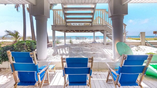 A covered outdoor seating area with blue chairs and a view of the beach. - Beachfront dog-friendly home with spacious decks and on-site pool (St. George Island)