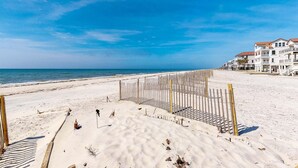 A beach with a wooden fence and a row of white buildings with red roofs in the background. - Beachfront dog-friendly home with spacious decks and on-site pool (St. George Island)