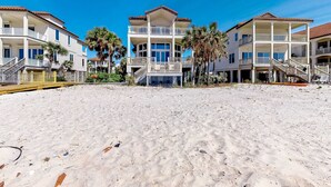 A beachfront property with multiple-story buildings, balconies, and a sandy beach. - Beachfront dog-friendly home with spacious decks and on-site pool (St. George Island)