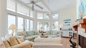 A spacious living room with a large window, a ceiling fan, and a fireplace. - Beachfront dog-friendly home with spacious decks and on-site pool (St. George Island)