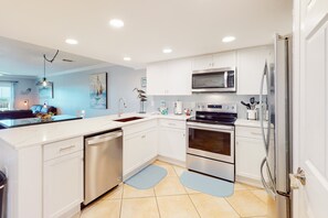 A modern kitchen with white cabinets, stainless steel appliances, and a large island with a sink. - Bright & comfortable gulf-side condo overlooking beach with WiFi, pool, central AC (Miramar Beach)