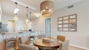 A dining area with a round table, wicker chairs, and a woven light fixture. - Newly-renovated top-floor condo with a beach & Gulf view, lagoon pool, & hot tub (Miramar Beach)