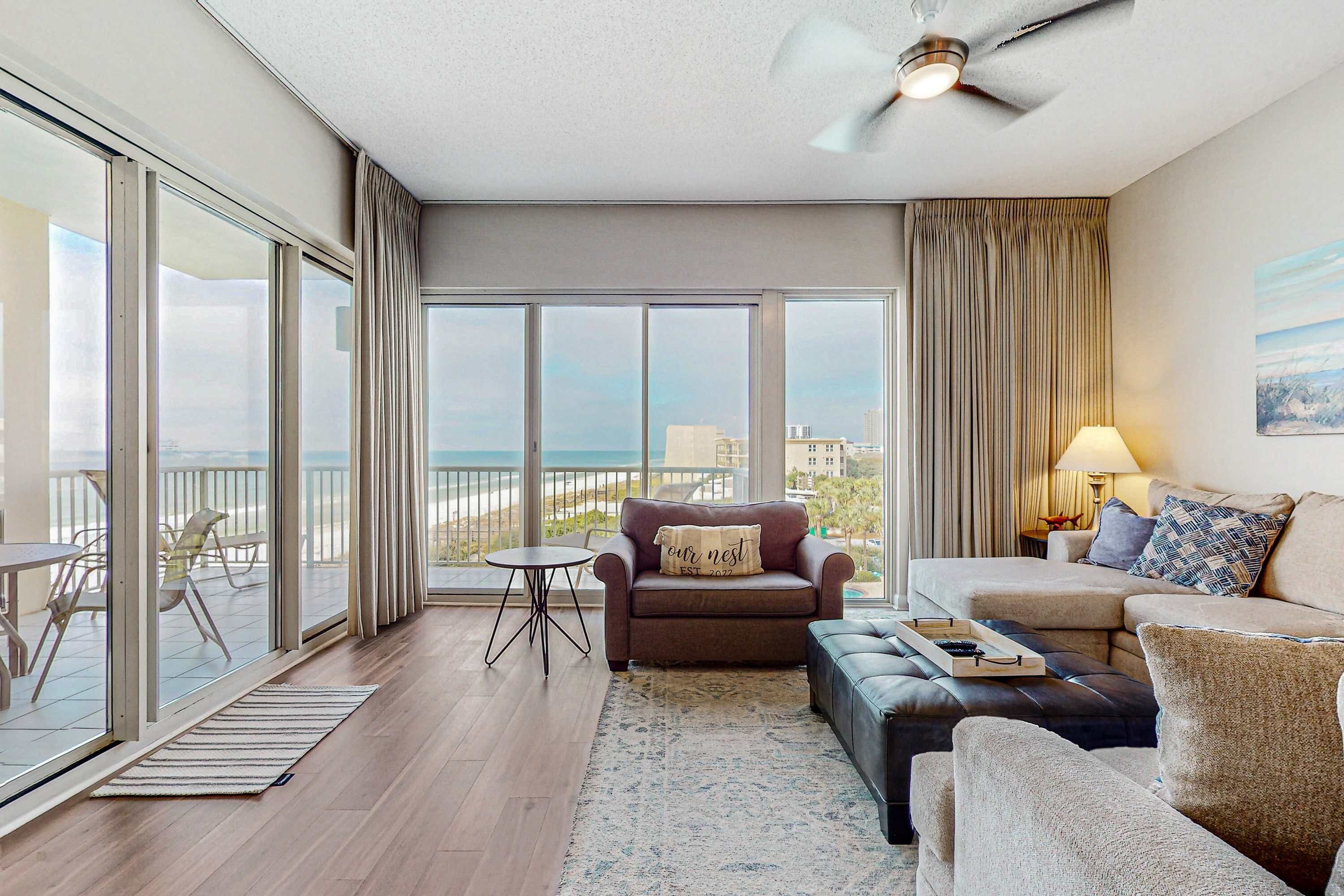 A spacious living room with a large sliding glass door leading to a balcony, a ceiling fan, and a sofa set with a tray of glasses.