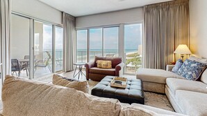 A spacious living room with a large sliding glass door leading to a balcony, a ceiling fan, and a view of the ocean. - Newly-renovated top-floor condo with a beach & Gulf view, lagoon pool, & hot tub (Miramar Beach)