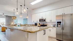 A modern kitchen with white cabinets, a granite countertop, stainless steel appliances, and pendant lighting. - Newly-renovated top-floor condo with a beach & Gulf view, lagoon pool, & hot tub (Miramar Beach)
