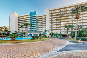 A hotel with a central pool, multiple balconies, and palm trees. - Beautiful, waterfront condo w a shared pool, gym, & beach access (Destin)