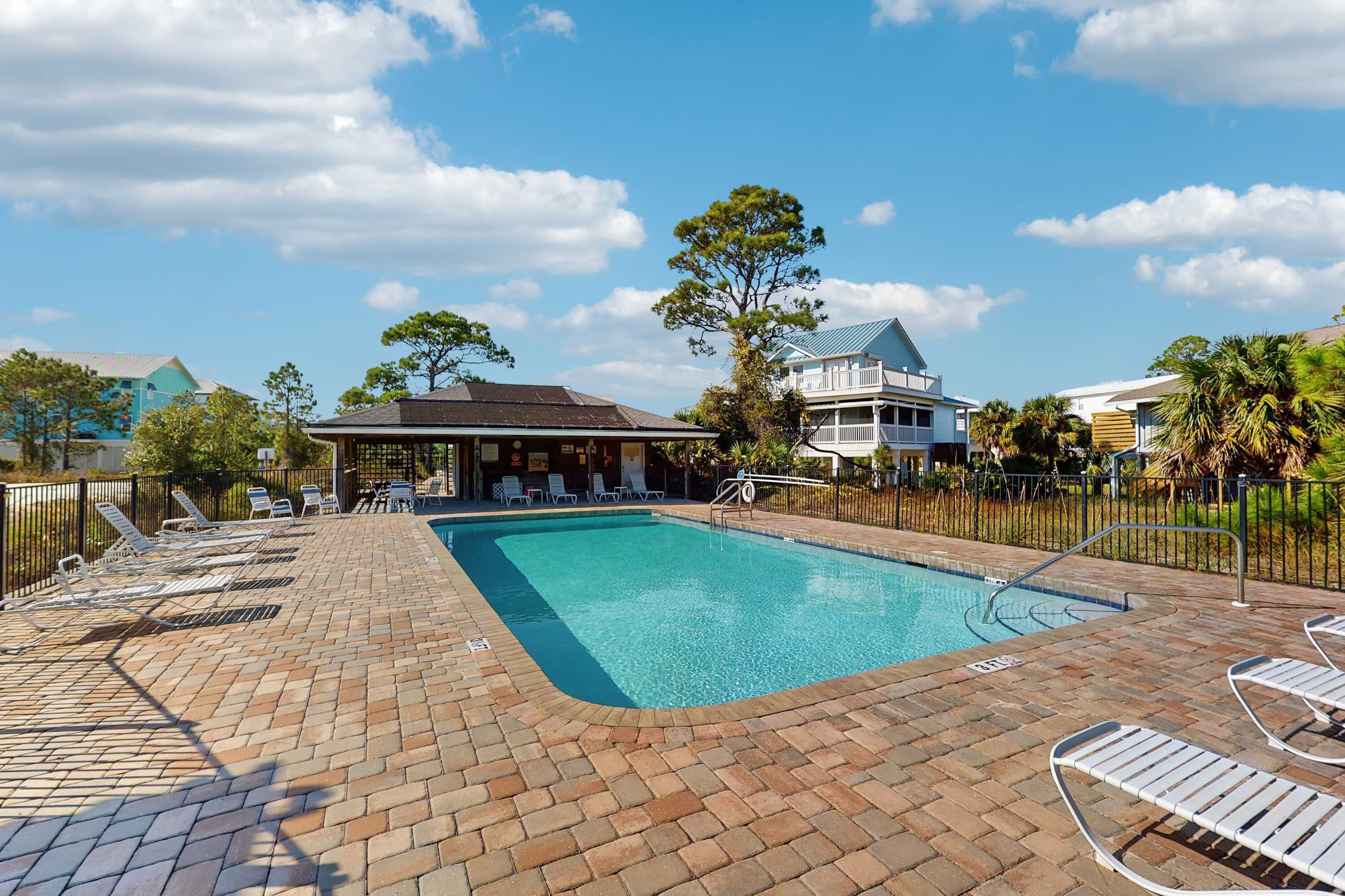 A rectangular swimming pool with a tiled deck, surrounded by lounge chairs and a fence.