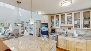 Une cuisine moderne dotée de plans de travail en granit, d’appareils électroménagers en acier inoxydable et d’armoires en bois clair.