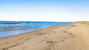 Une plage avec un large rivage sablonneux, des vagues douces et un ciel bleu dégagé.
