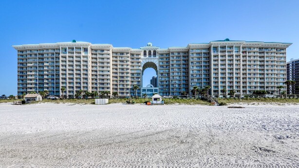 Un grande hotel a più piani con un ingresso ad arco centrale, situato su una spiaggia sabbiosa.
