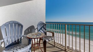 Un balcone con due sedie e un tavolino, vista sulla spiaggia e una ringhiera.
