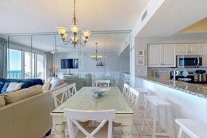 Una cocina moderna con armarios blancos, un microondas y una mesa de comedor de vidrio con sillas blancas.