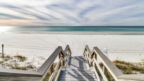 Eine Holztreppe führt zu einem Strand unter blauem Himmel.