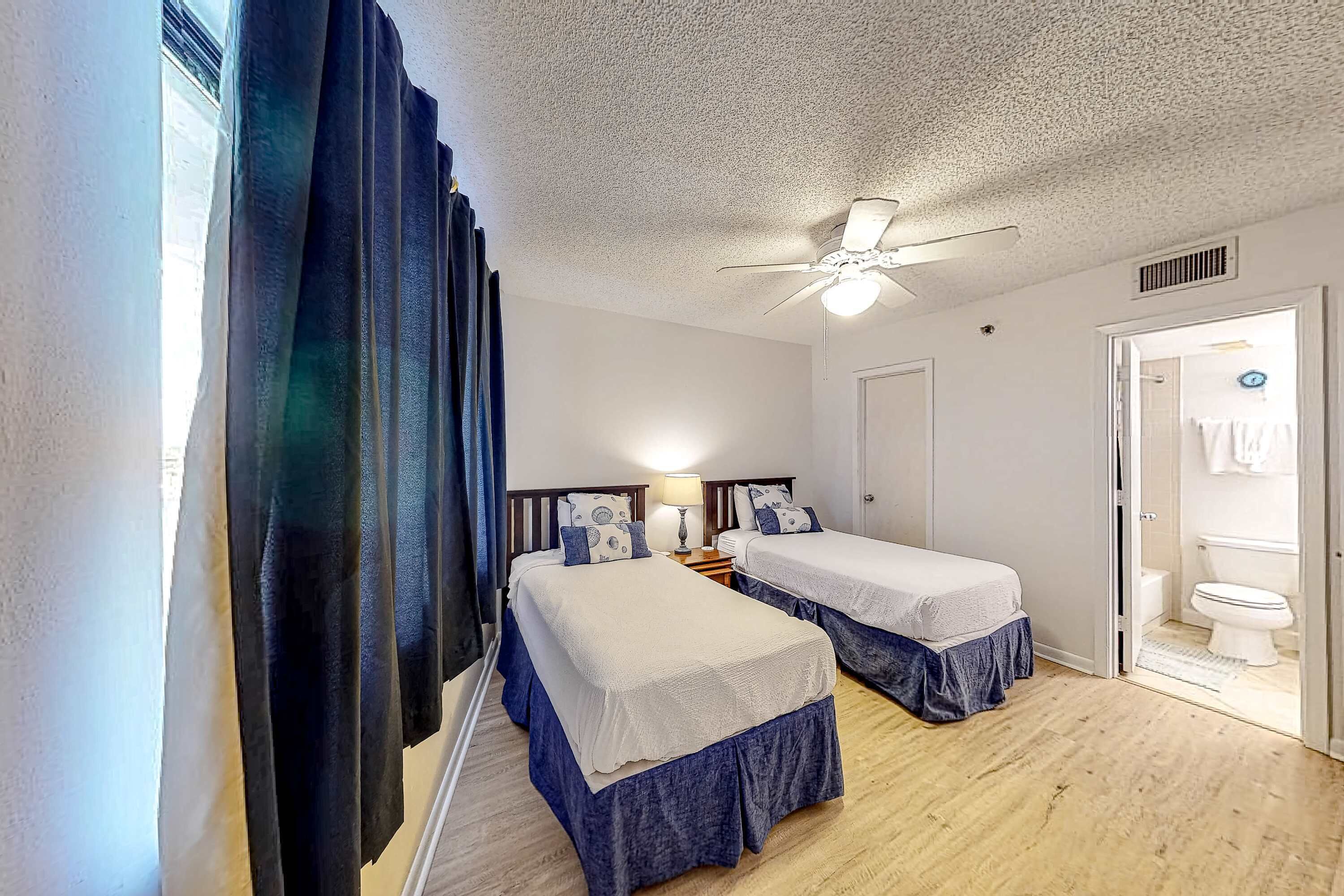 A hotel room with two beds, a ceiling fan, a nightstand, and a view of the bathroom.