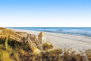 Un escalier en bois mène à une zone de plage où se trouve un poste de surveillance pour les sauveteurs.