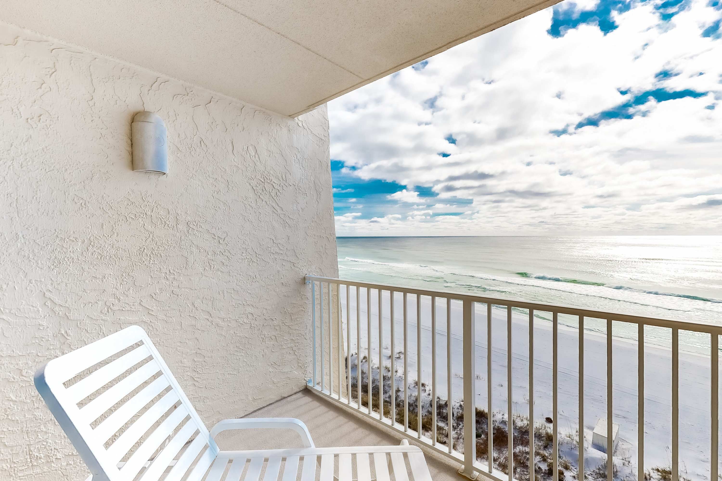 A balcony with a white railing, a white chair, and a textured wall.