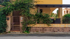 A building with a yellow facade, a brick lower section, and a metal gate. - Holiday Home 'La Casa Del Bouganville' Near Beaches with Courtyard & Air Conditioning (Golfo Aranci)