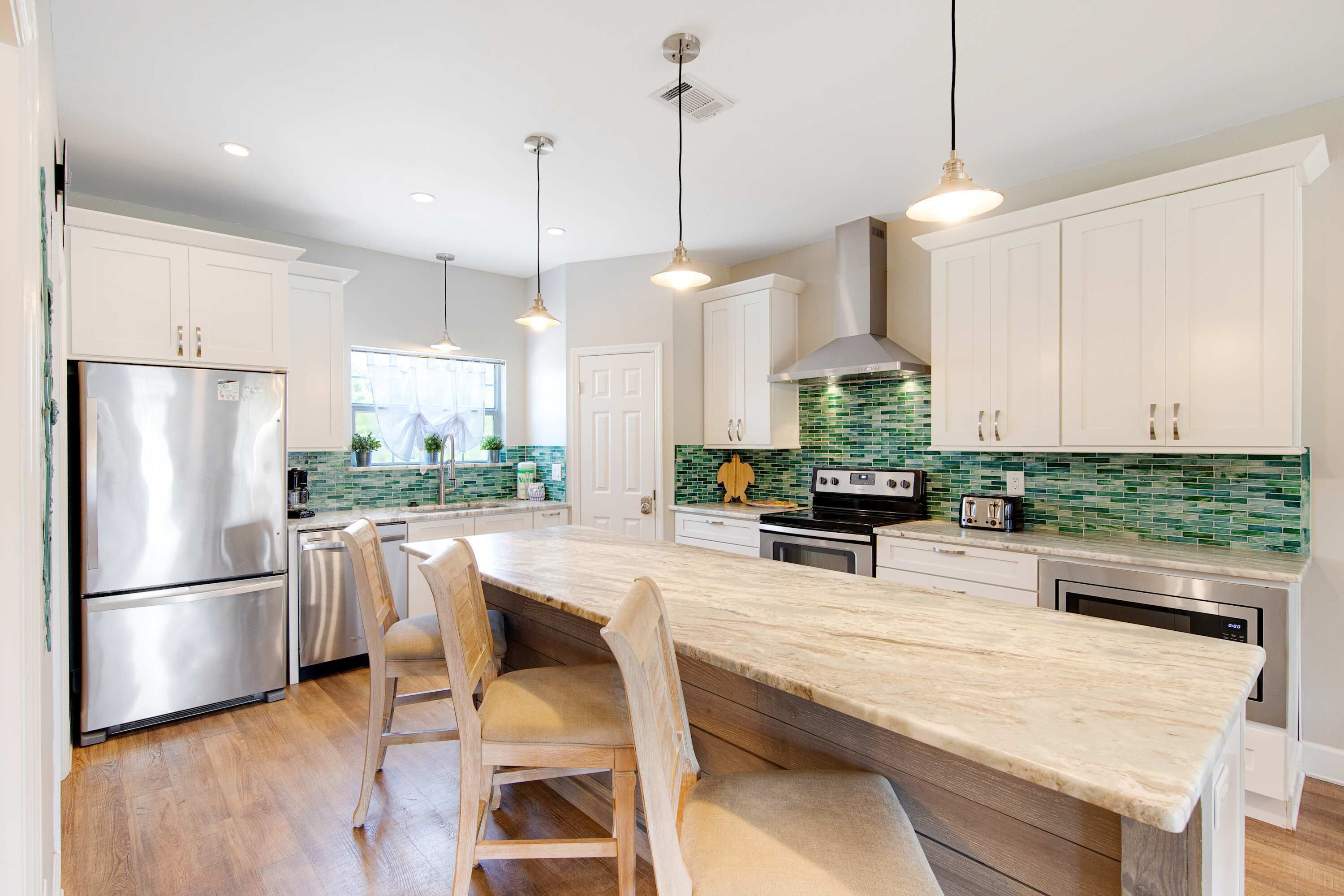 Una cocina moderna con armarios blancos, un refrigerador de acero inoxidable, una isla grande con taburetes y luminarias colgantes.