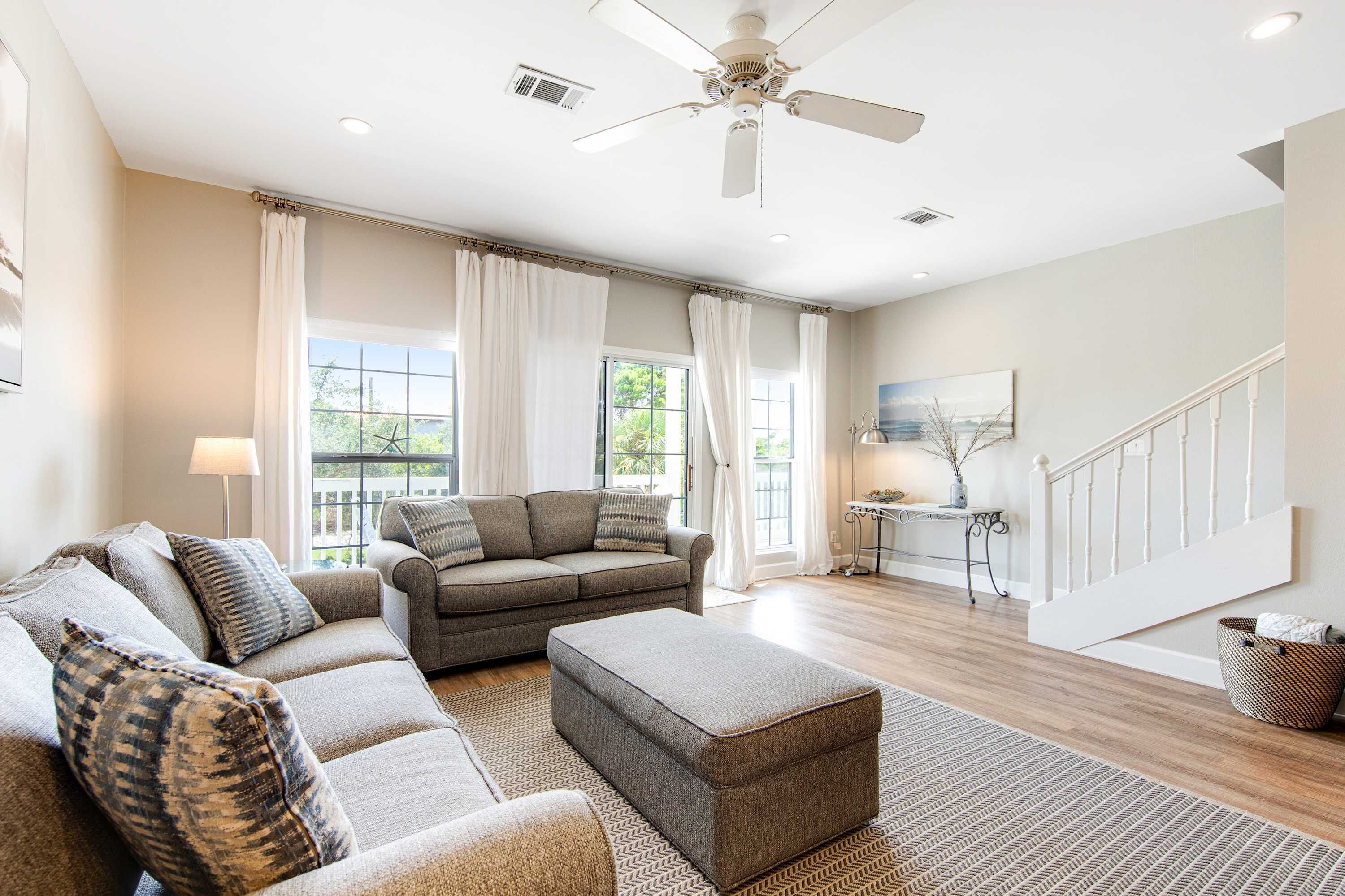 A spacious living room with a grey sectional sofa, a matching ottoman, and a ceiling fan.