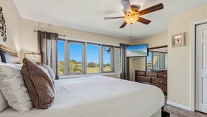 Een slaapkamer met een groot bed, een plafondventilator, een dressoir, een televisie en uitzicht op de omgeving.