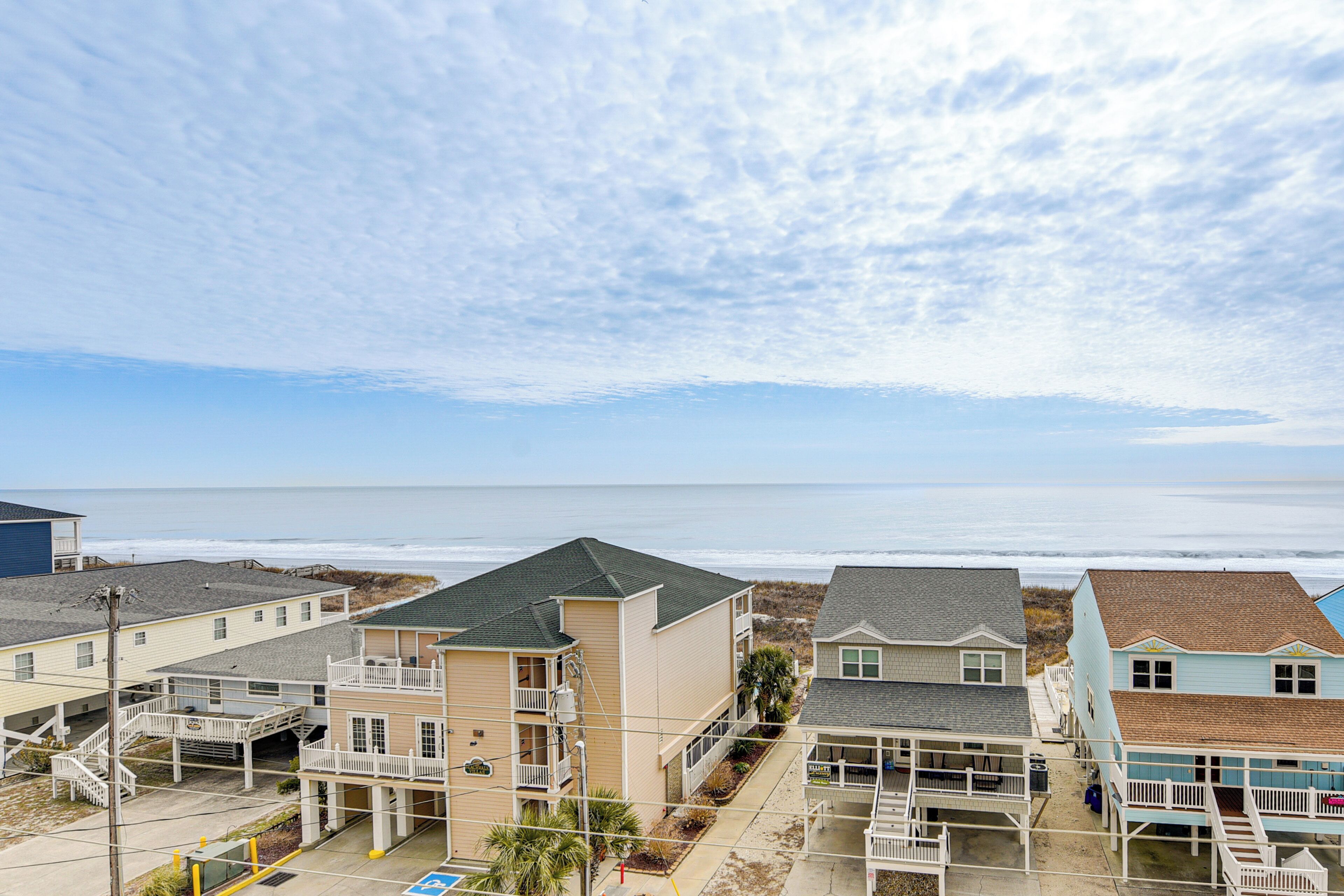 A beachfront hotel with multiple buildings, including a two-story structure with a balcony and a single-story building with a porch.