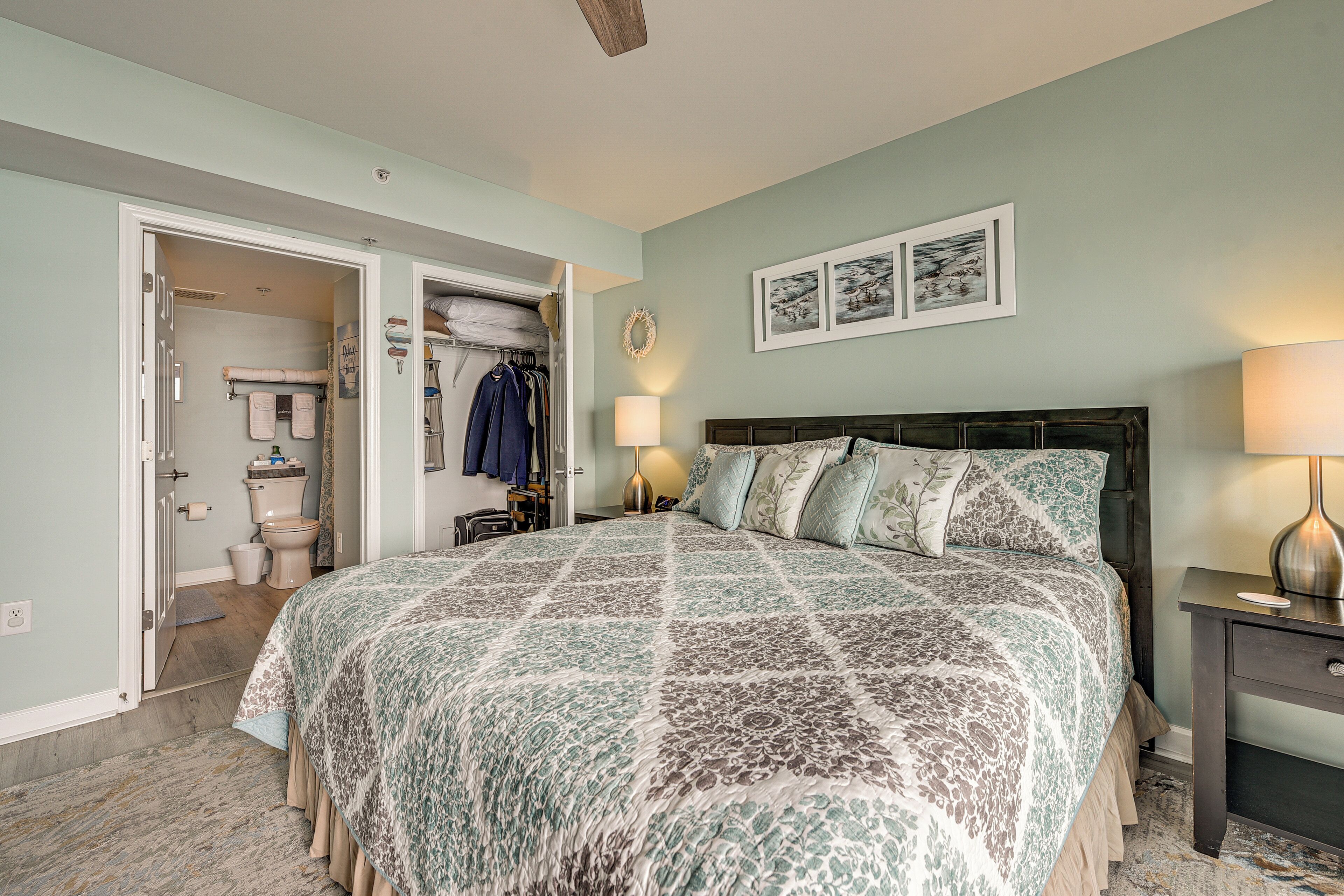 A bedroom with a large bed, a nightstand, a closet, and a bathroom visible through an open door.