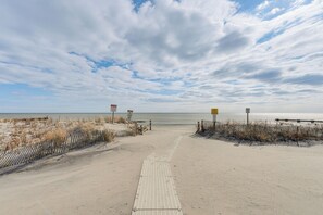 Ein sandiger Strand mit einem gepflasterten Weg zum Wasser, umgeben von Dünen und Schildern.