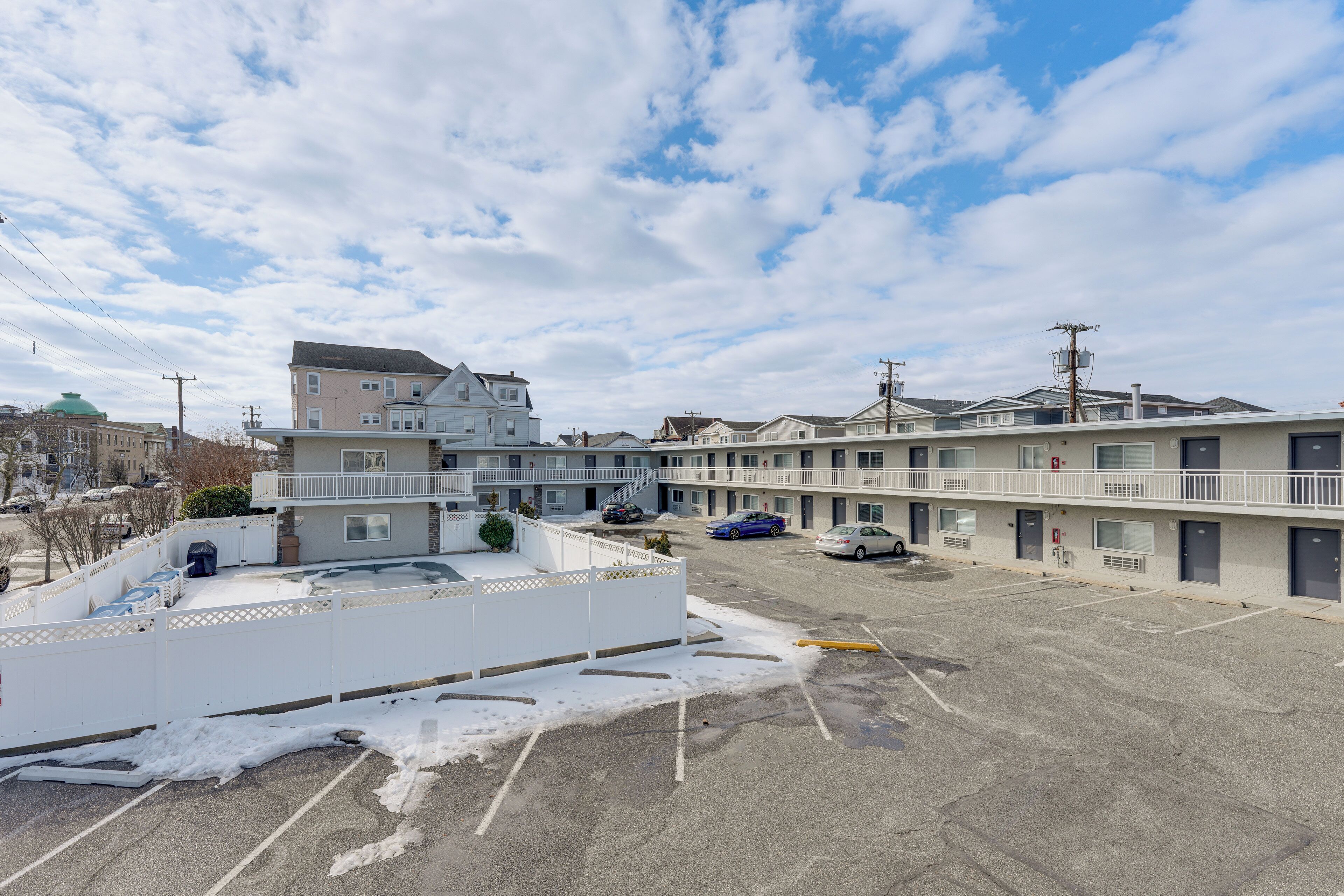 A multi-story motel with a parking lot, some snow on the ground, and a clear sky.