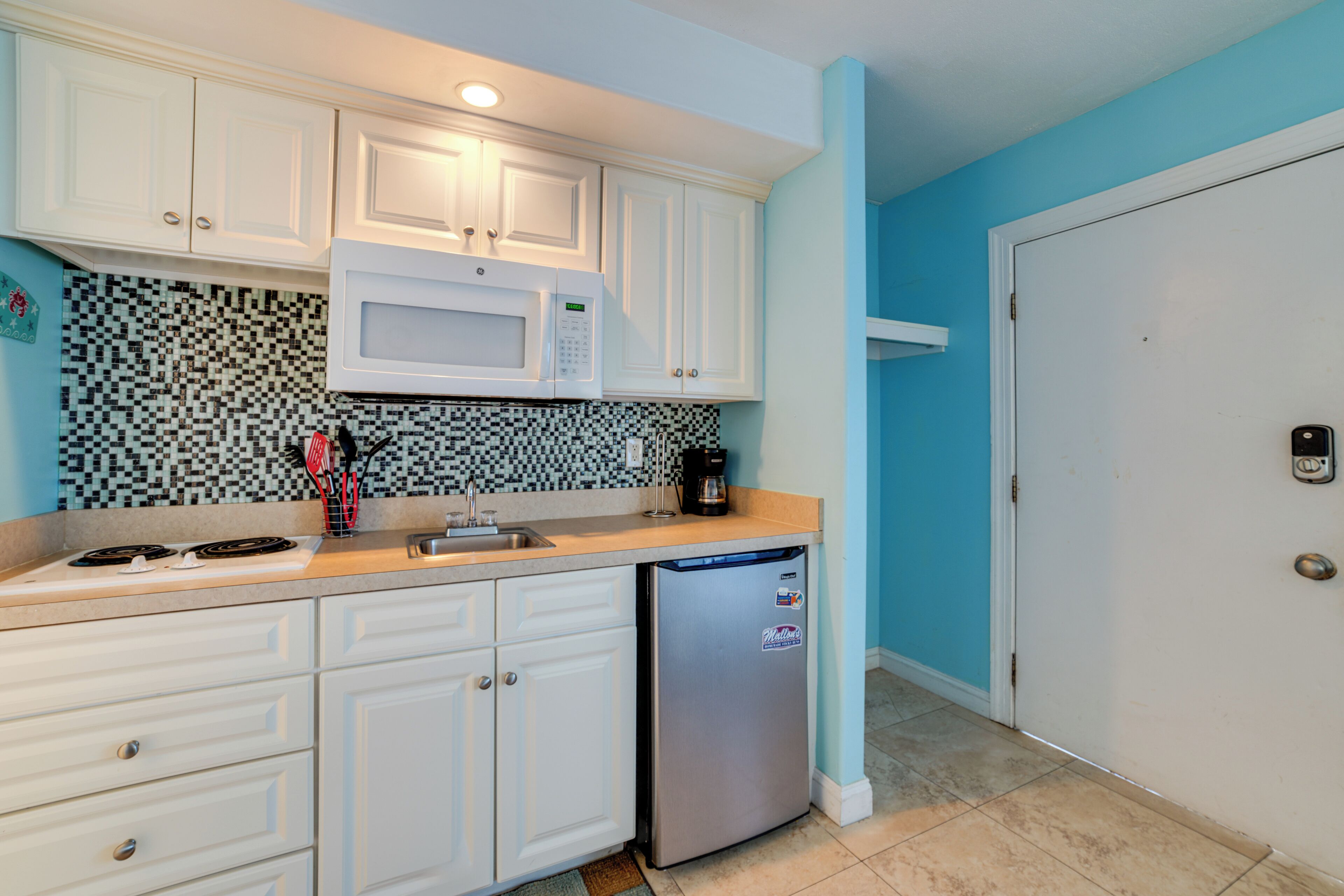 A compact kitchen with white cabinets, a microwave, a refrigerator, and a tiled backsplash.