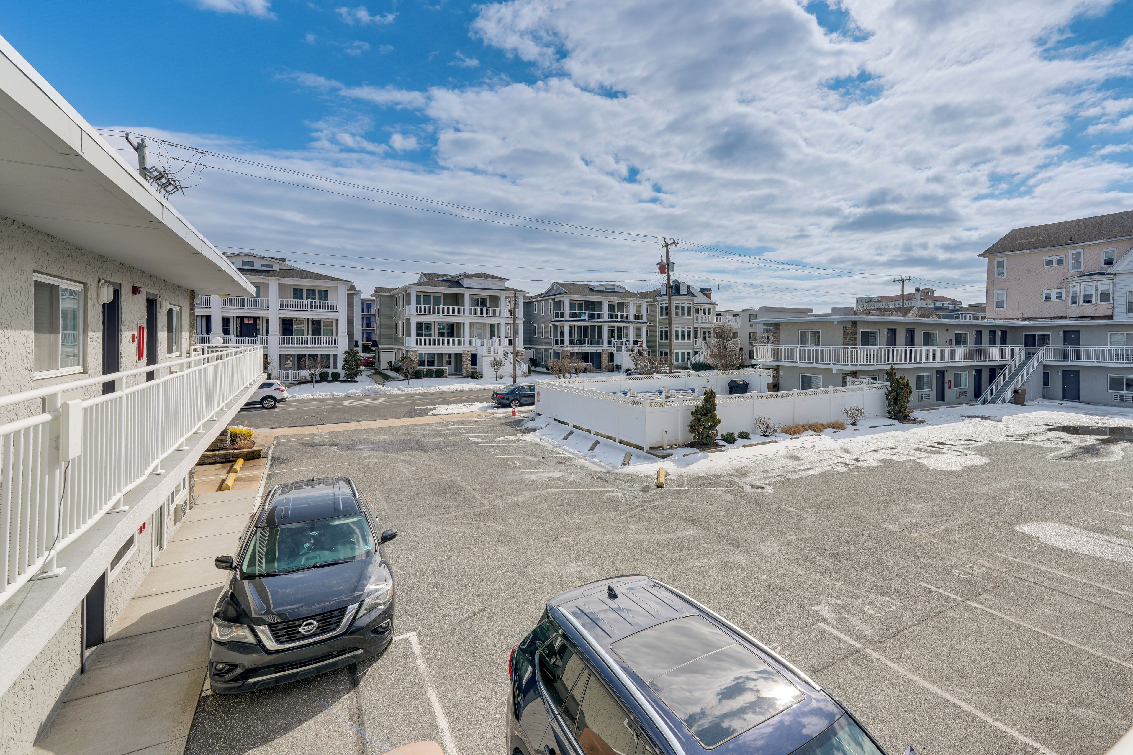 A parking lot with several cars, a building with balconies, and a clear sky.