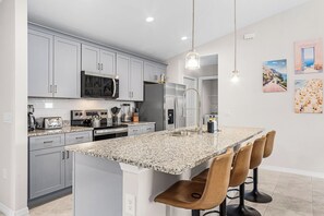 A modern kitchen with grey cabinets, stainless steel appliances, a granite countertop, and a bar area with bar stools. - Canal-front Fun! Fish & Relax in Cape Coral (Cape Coral)