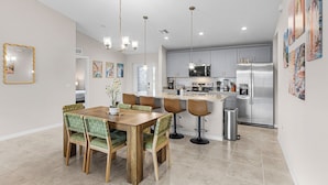 A modern kitchen with grey cabinets, stainless steel appliances, and a dining area with wooden table and green upholstered chairs. - Canal-front Fun! Fish & Relax in Cape Coral (Cape Coral)