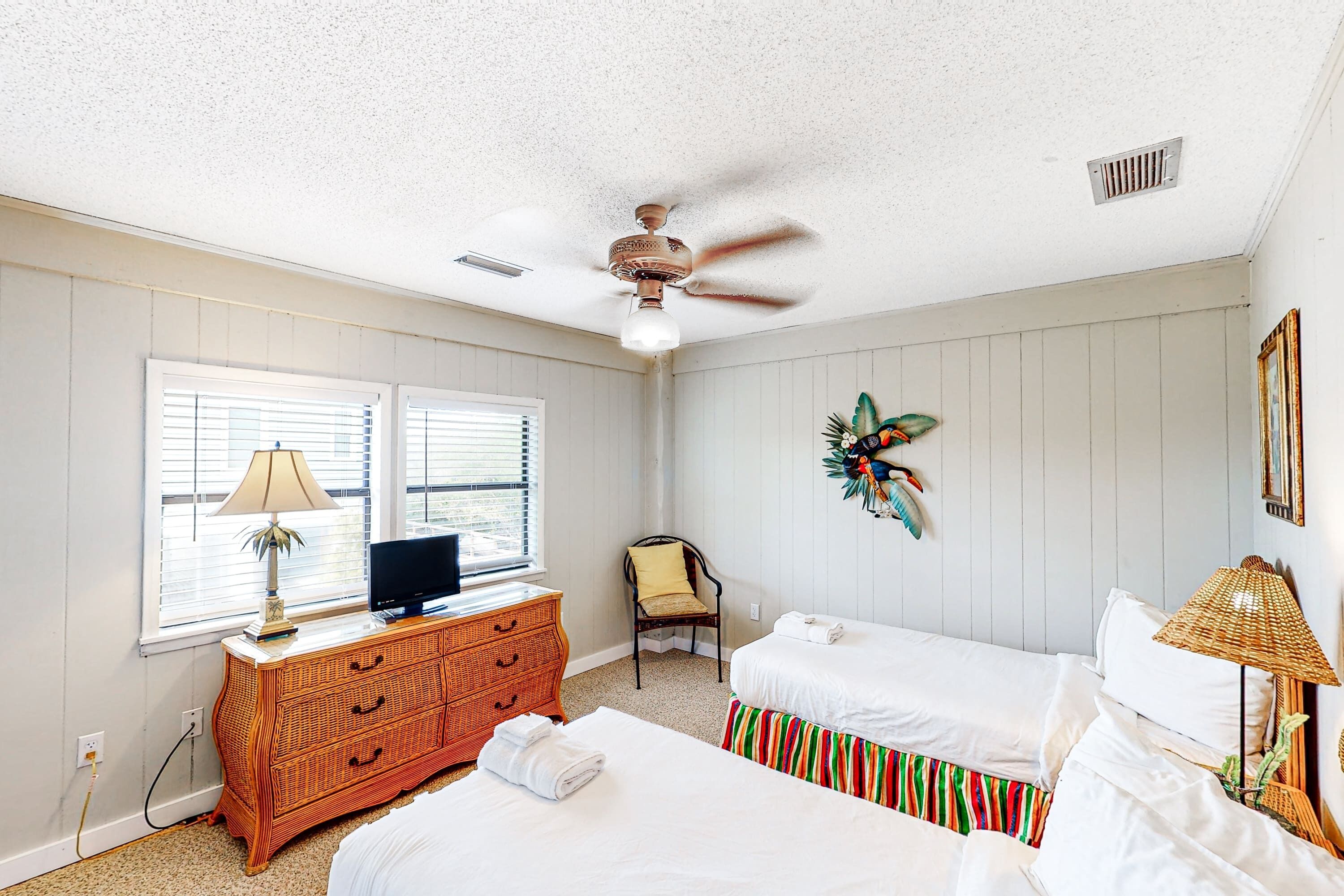 A bedroom with two beds, a TV on a dresser, a ceiling fan, and a window with blinds.