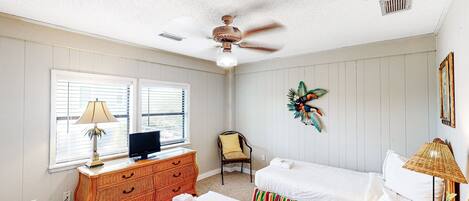 A bedroom with two beds, a TV on a dresser, a ceiling fan, and a window with blinds.