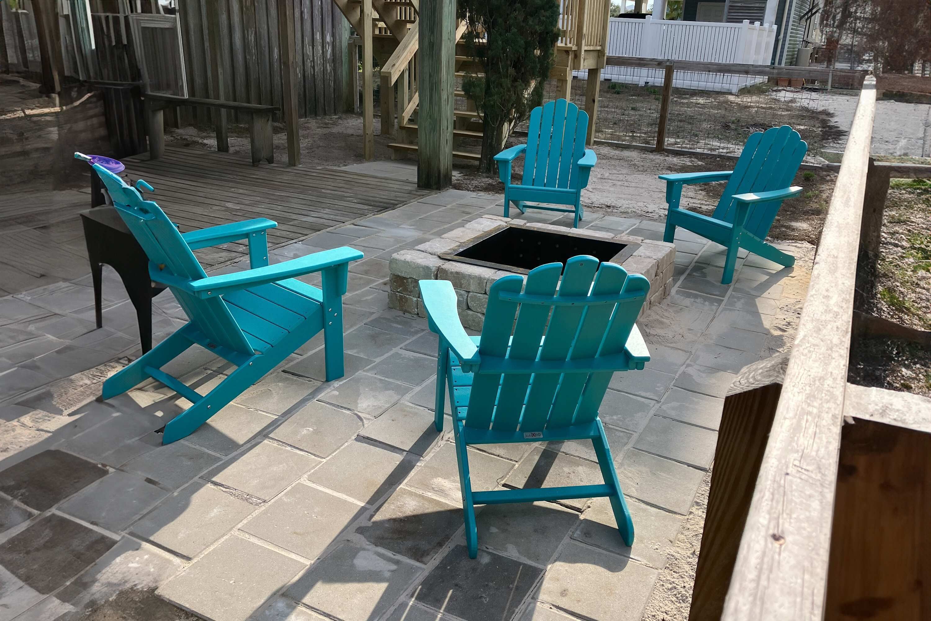 A patio area with four turquoise Adirondack chairs arranged around a stone fire pit.