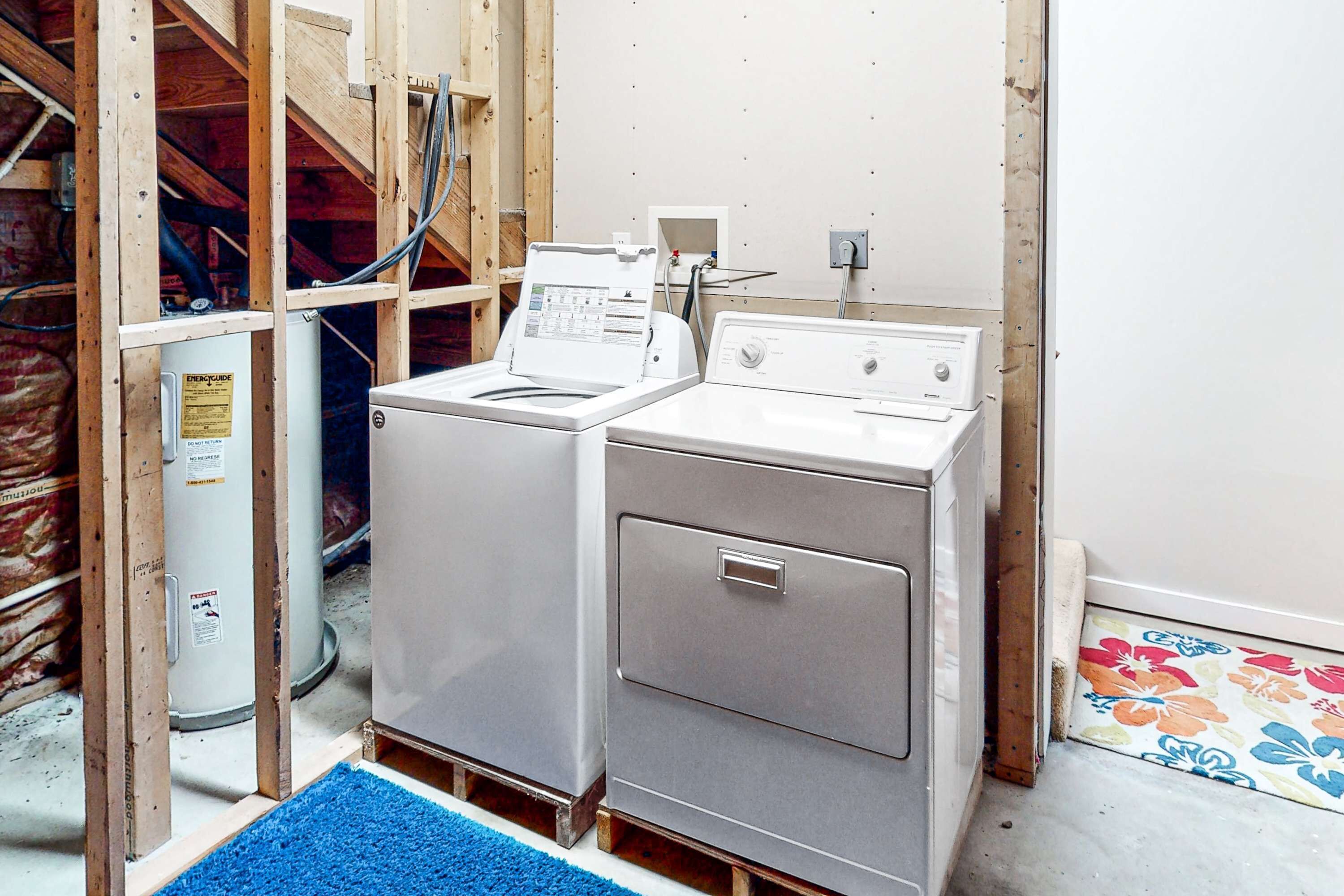 A laundry room with two stacked washers and dryers, a blue mat, and exposed wooden framing.