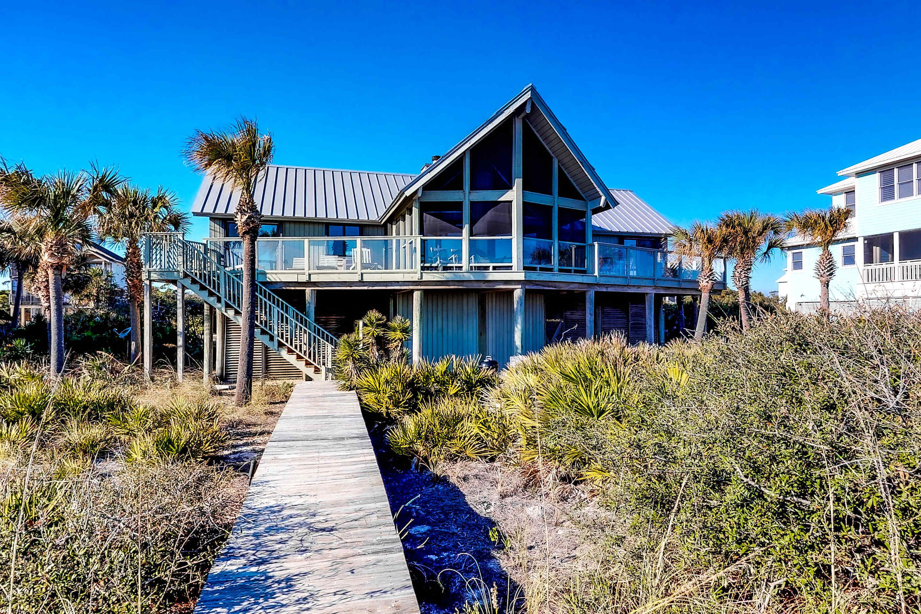 Une maison située en bord de mer, dotée d’un balcon, d’une allée couverte et de palmiers.