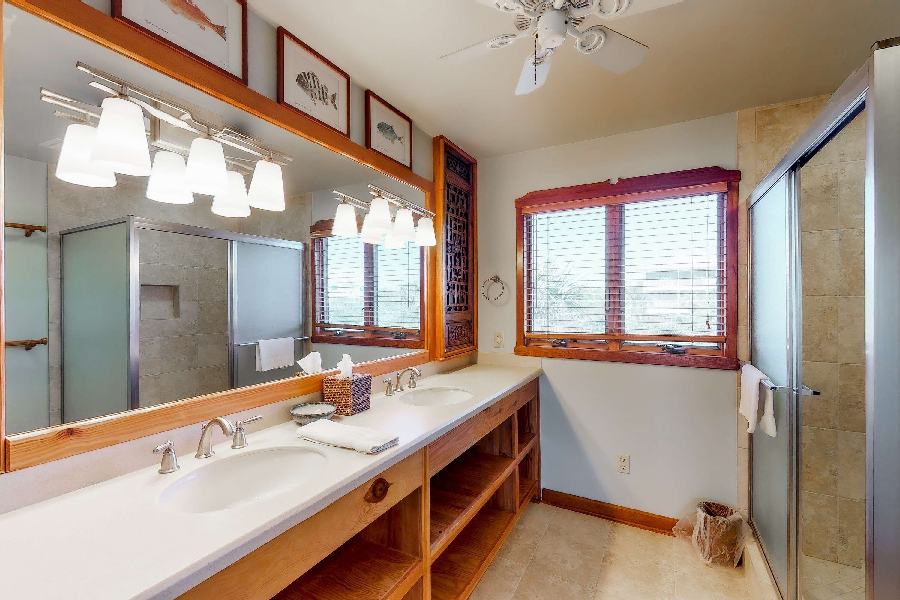 A bathroom with a large mirror, two sinks, a shower, and a ceiling fan.