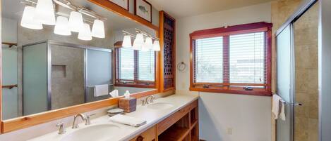 A bathroom with a large mirror, two sinks, a shower, and a ceiling fan.