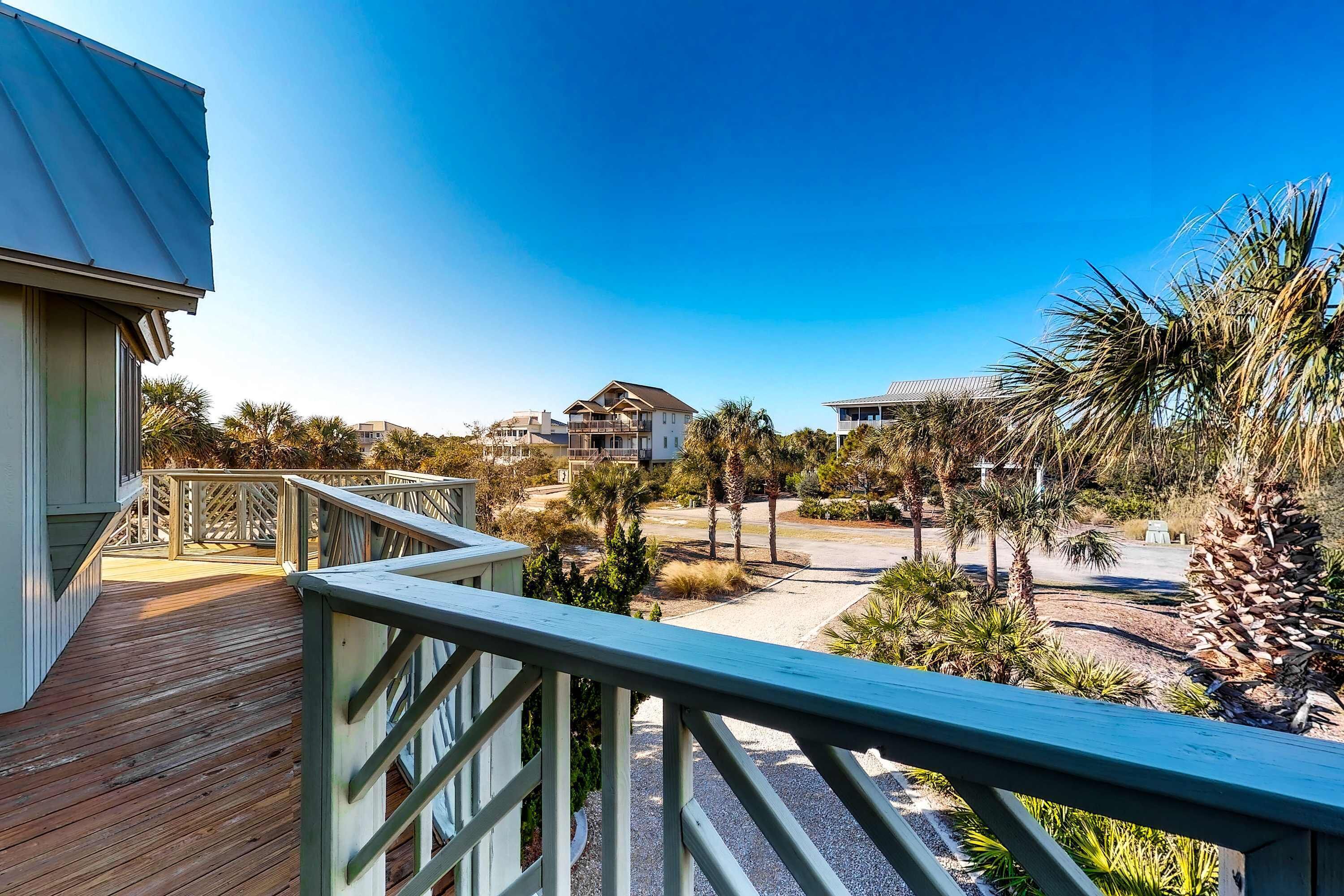 A wooden deck with a railing, overlooking a residential area with houses and palm trees.