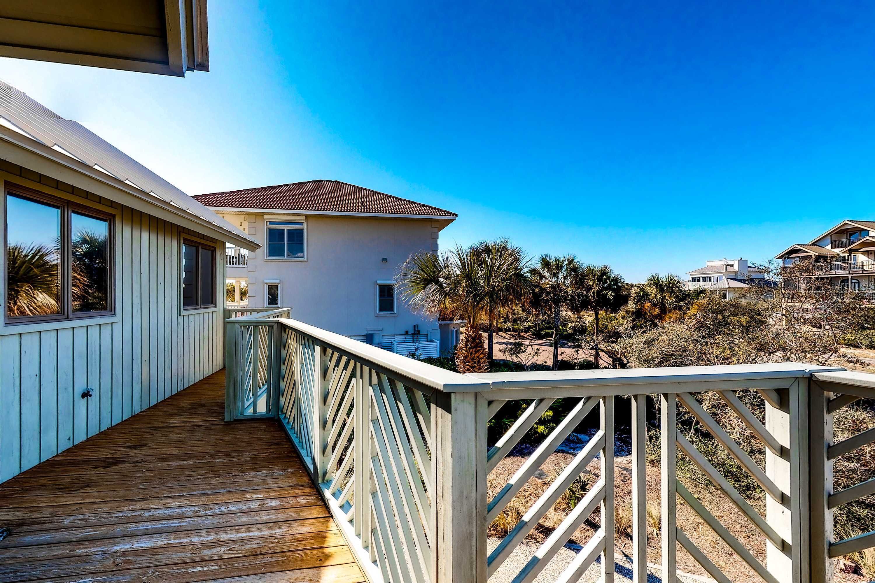 A wooden deck with a railing, a building with a tiled roof, and a clear blue sky.