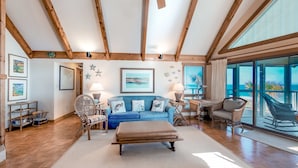 A spacious living room with a blue sofa, wicker chairs, a wooden ceiling, and large windows. - Snowbird-friendly beachfront home with a pool, tennis, washer/dryer, fireplace (St. George Island)