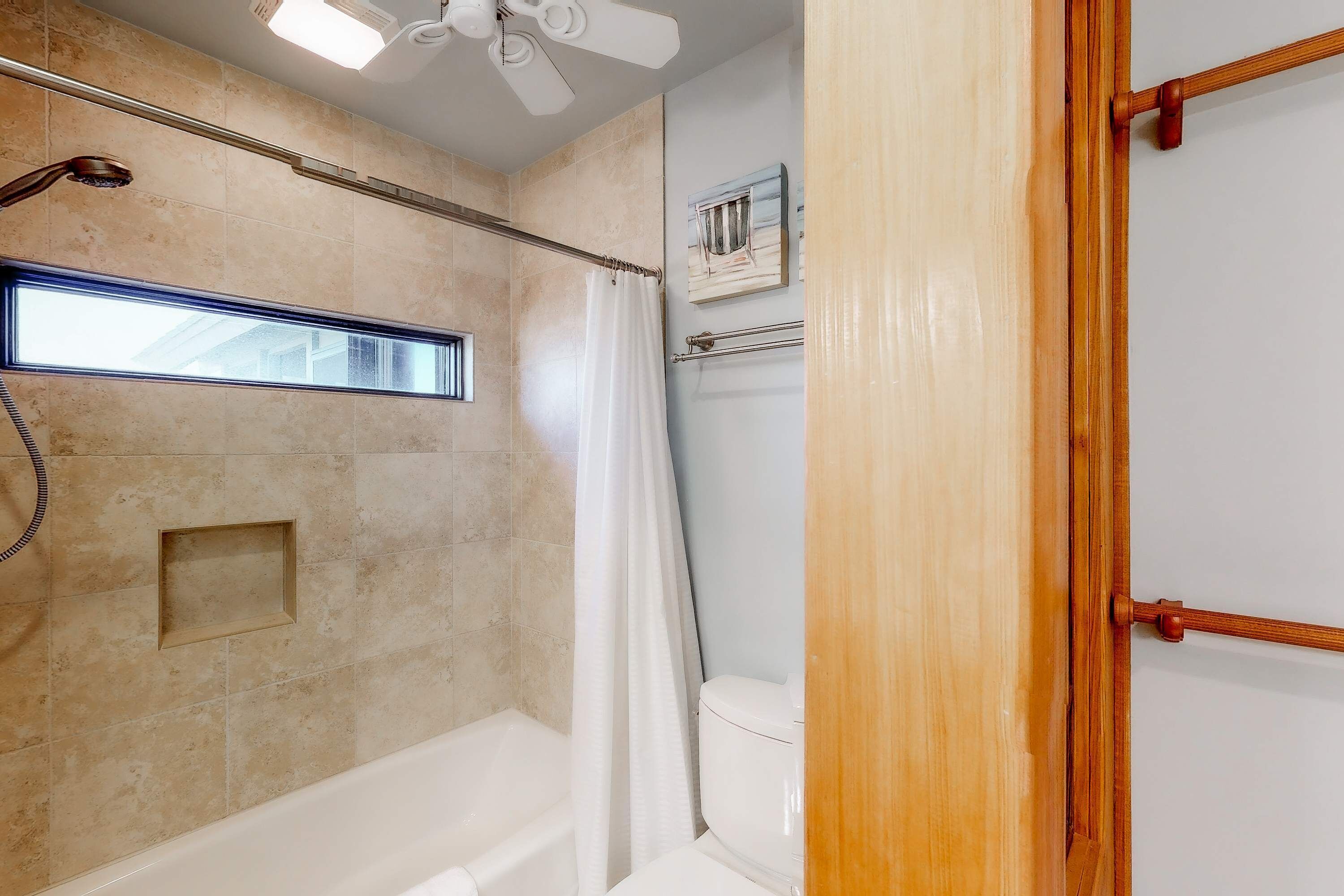 A bathroom with a shower, a toilet, and a window.