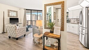 A modern living room with a sofa, a TV, a lamp, and a large mirror. - Beautiful condo w/ shared pool, hot tub, tennis, gym & gorgeous beach views (Miramar Beach)