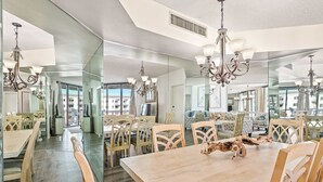 A spacious dining area with a large table and chairs, a chandelier, and a view through large windows. - Beautiful condo w/ shared pool, hot tub, tennis, gym & gorgeous beach views (Miramar Beach)