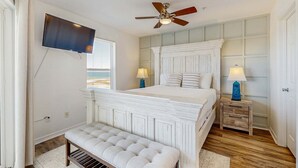Ein Schlafzimmer mit einem großen Bett, einem Deckenventilator, einem Fernseher und Meerblick.