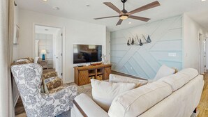 Ein Wohnzimmer mit einer Couch, einem gemusterten Sessel, einem Fernseher und einem Deckenventilator.