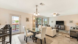 Un salón amplio con una mesa de comedor de cristal, sofás blancos, un televisor de pantalla plana y un balcón con vistas.